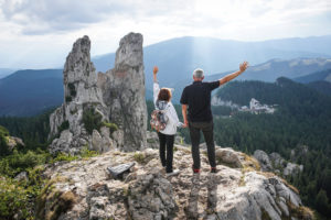 Color picture of an elderly couple holding hands and waving on top of a mountain